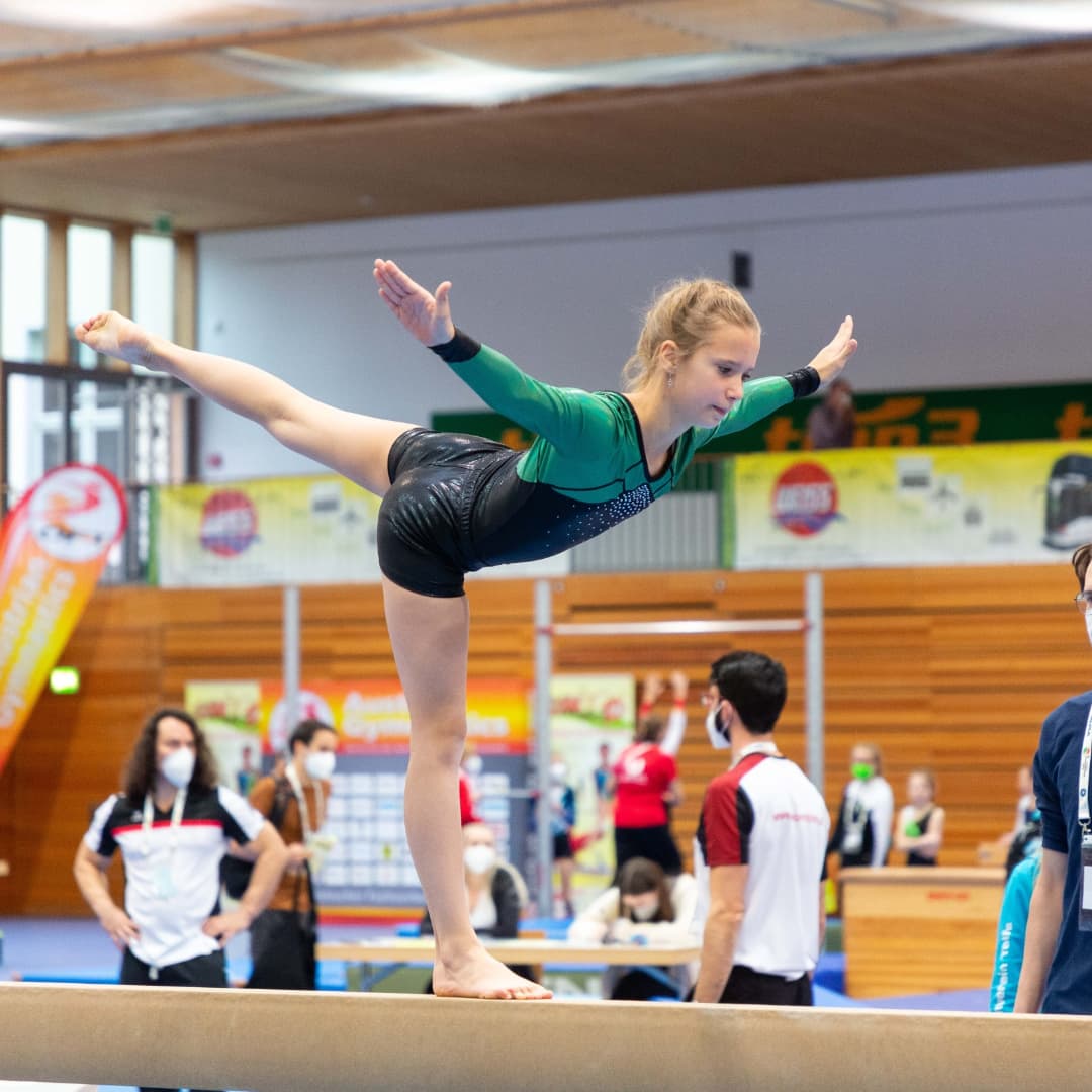 Ein junges Mädchen balanciert in einer Turnhalle auf dem Schwebebalken.
