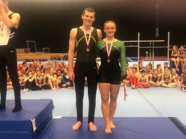 Ein Mann und eine Frau stehen auf einem Podium mit Medaillen um den Hals