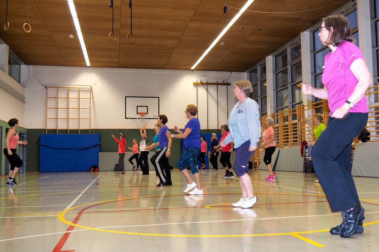 Eine Gruppe von Leuten tanzt in einer Turnhalle.