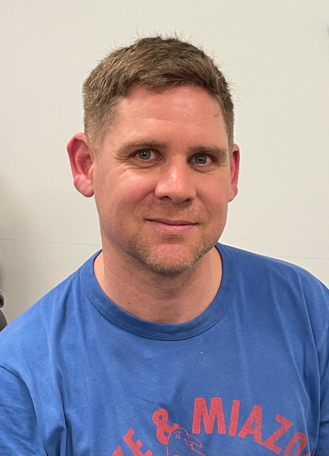 Eine Frau sitzt mit gefalteten Händen an einem Tisch und lächelt.