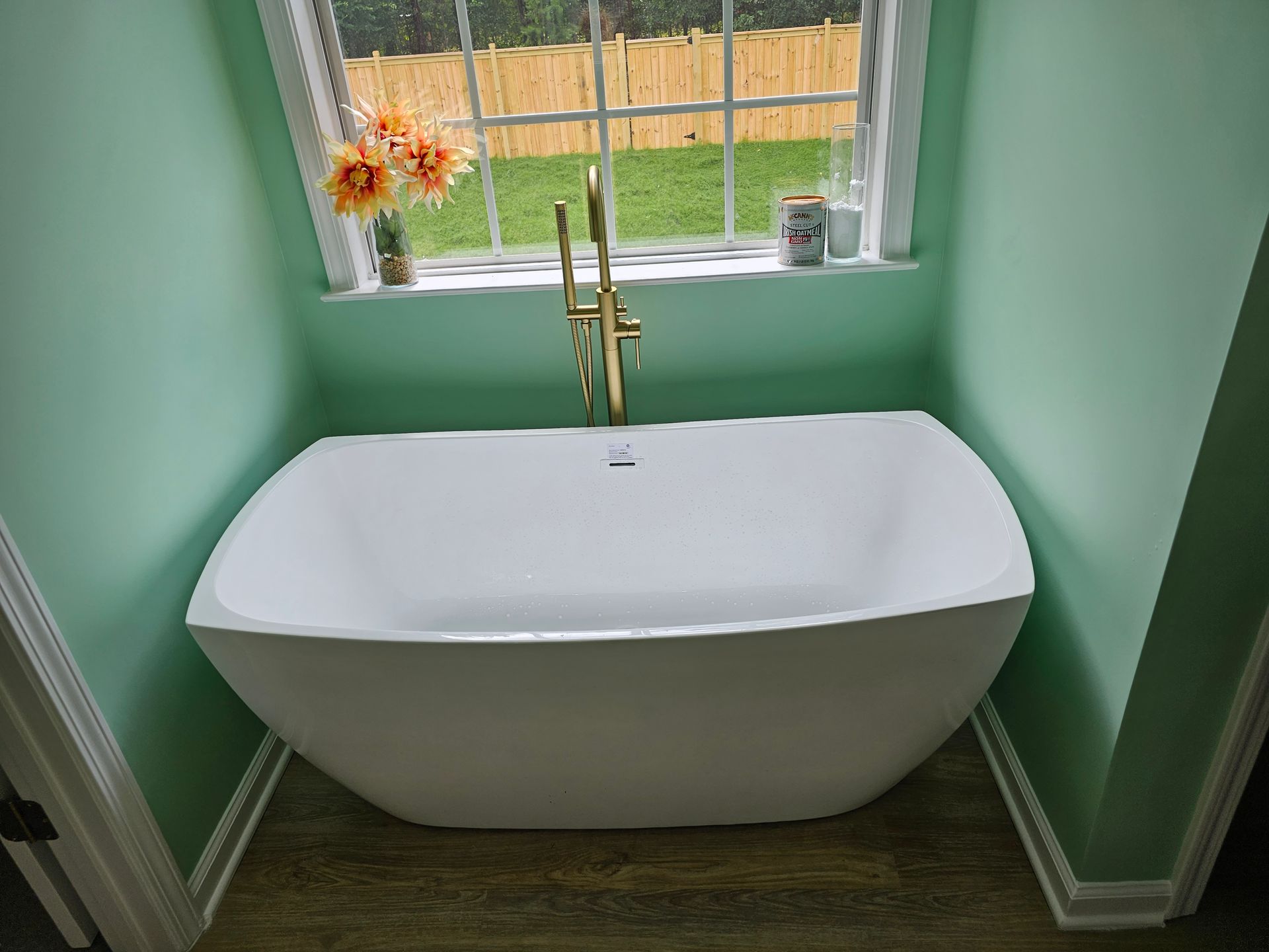 Construction worker repairing a window on a gray house exterior next to a white fence.