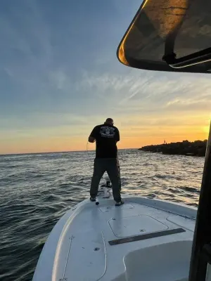 Person standing on the bow of a boat at sunset, looking out over calm water.
