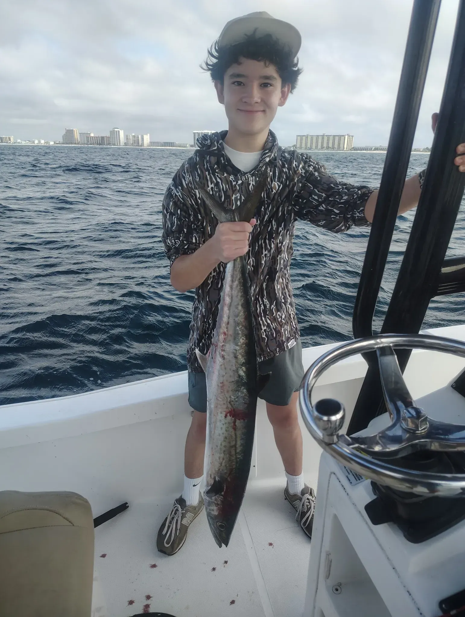 Person on a boat holding a large fish with ocean and distant shoreline in the background