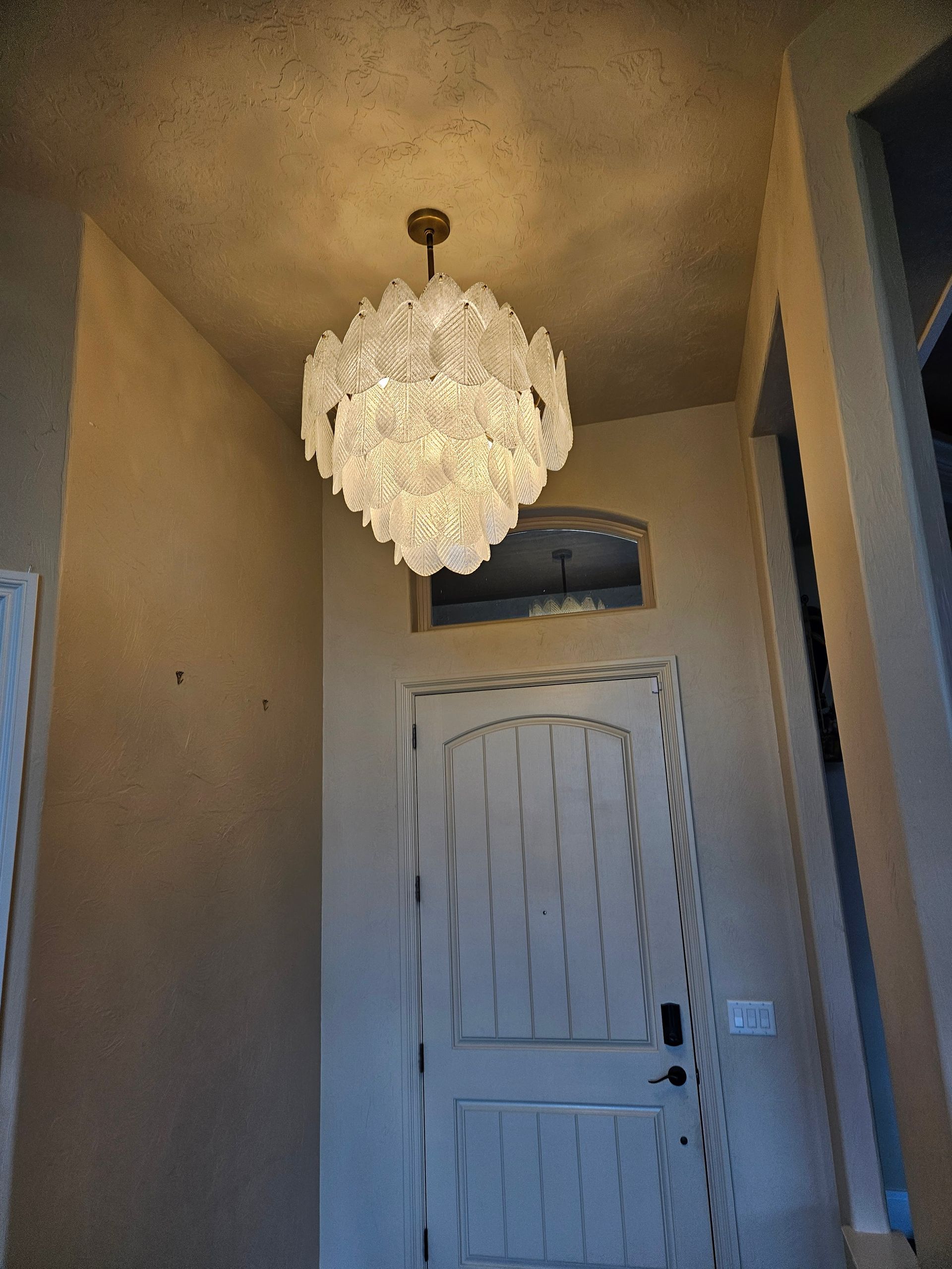 Crystal chandelier hanging above a white wooden door in a beige hallway.