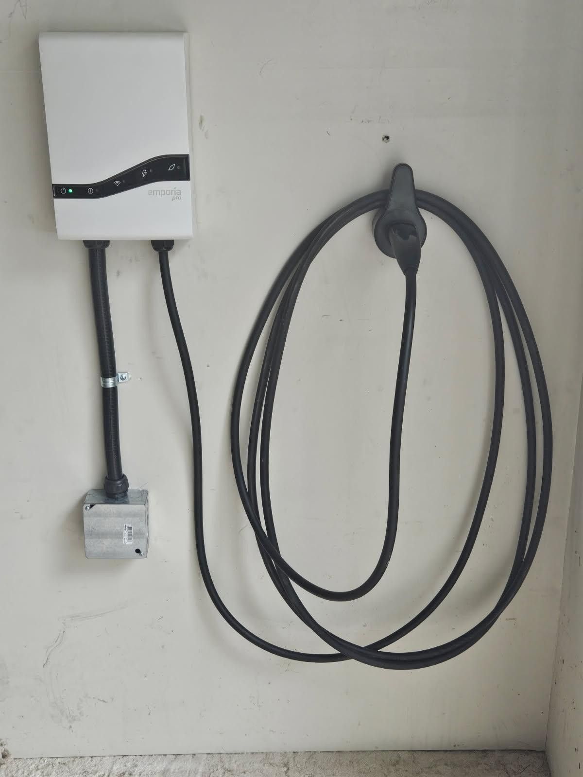 White wall-mounted electric vehicle charger with coiled black cable and charging plug.
