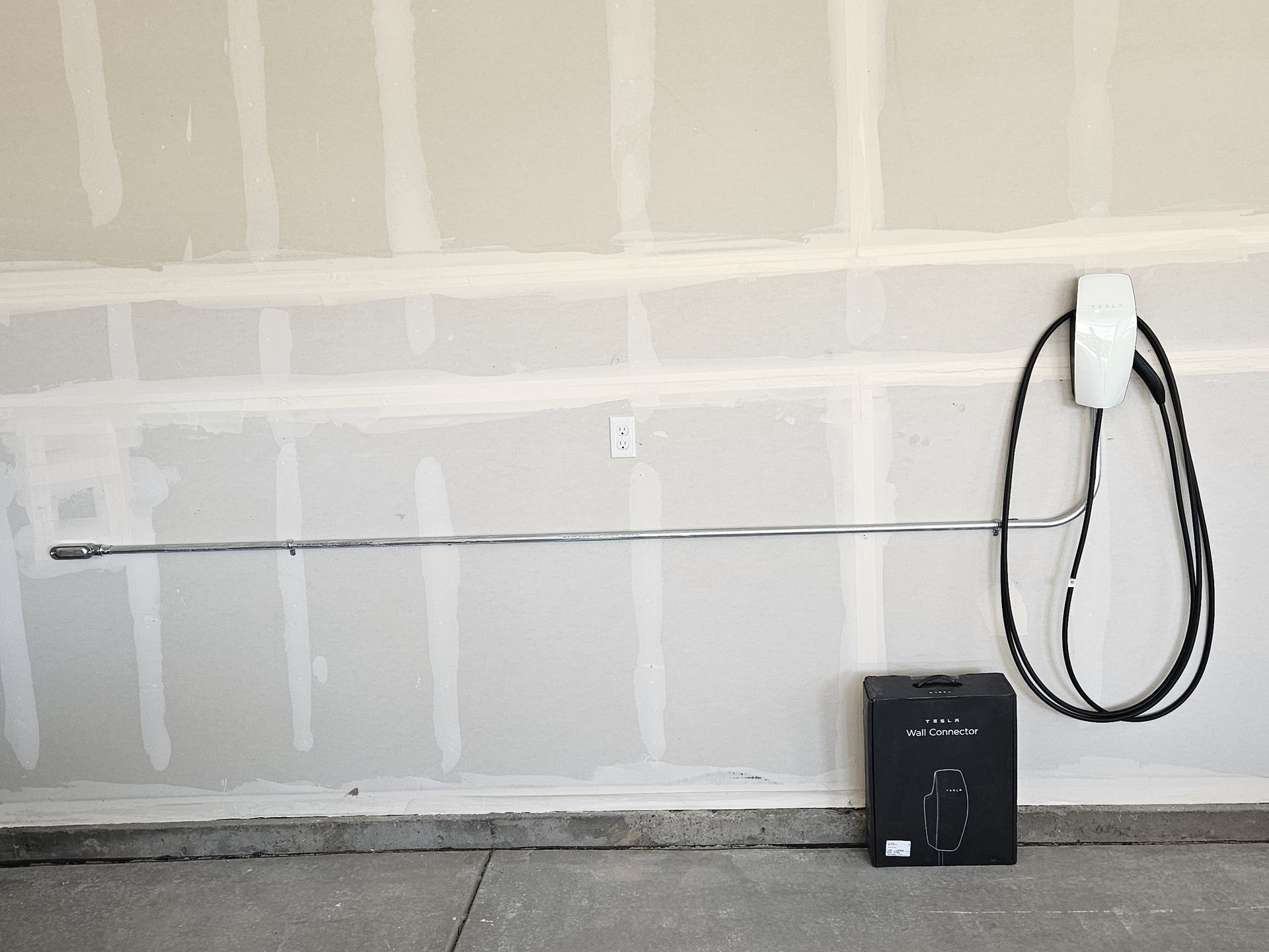 Electric vehicle charger installed on a garage wall, with conduit and charging cable.