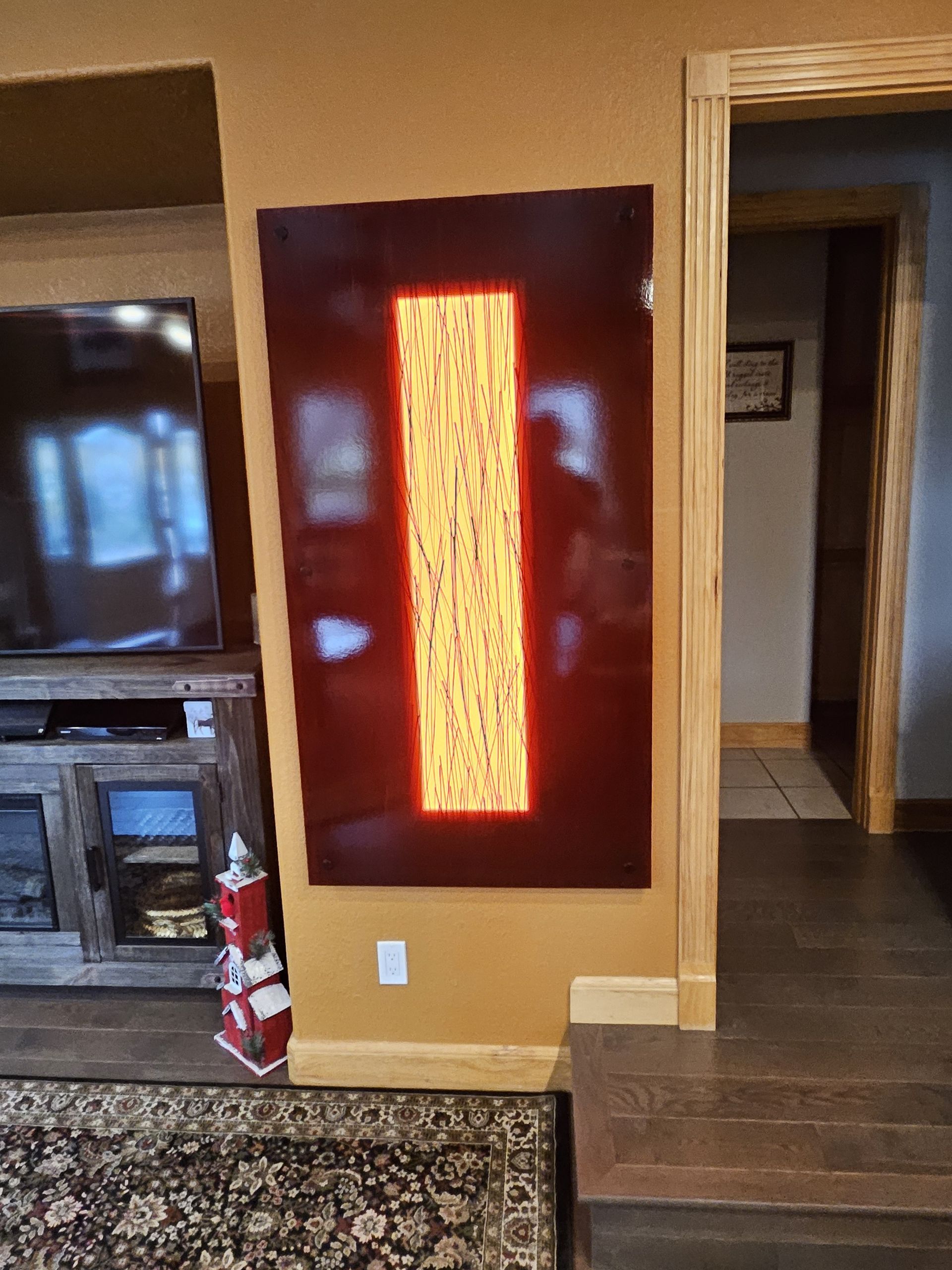 Large, rectangular artwork on a wall. It has a dark red border and an inner yellow/orange illuminated vertical rectangle.