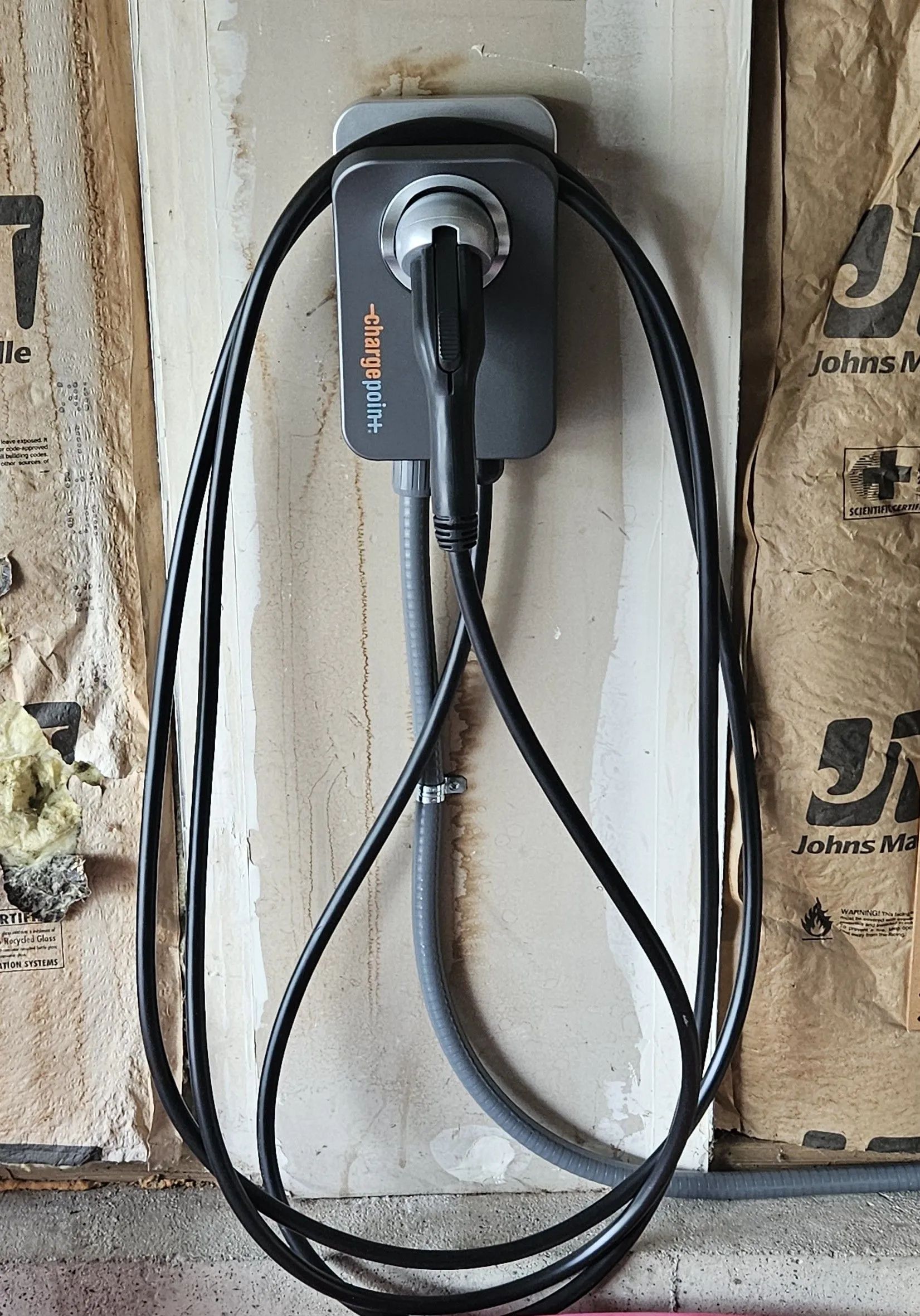 EV charger mounted on a wall with a looped black cable. The charger is plugged in.