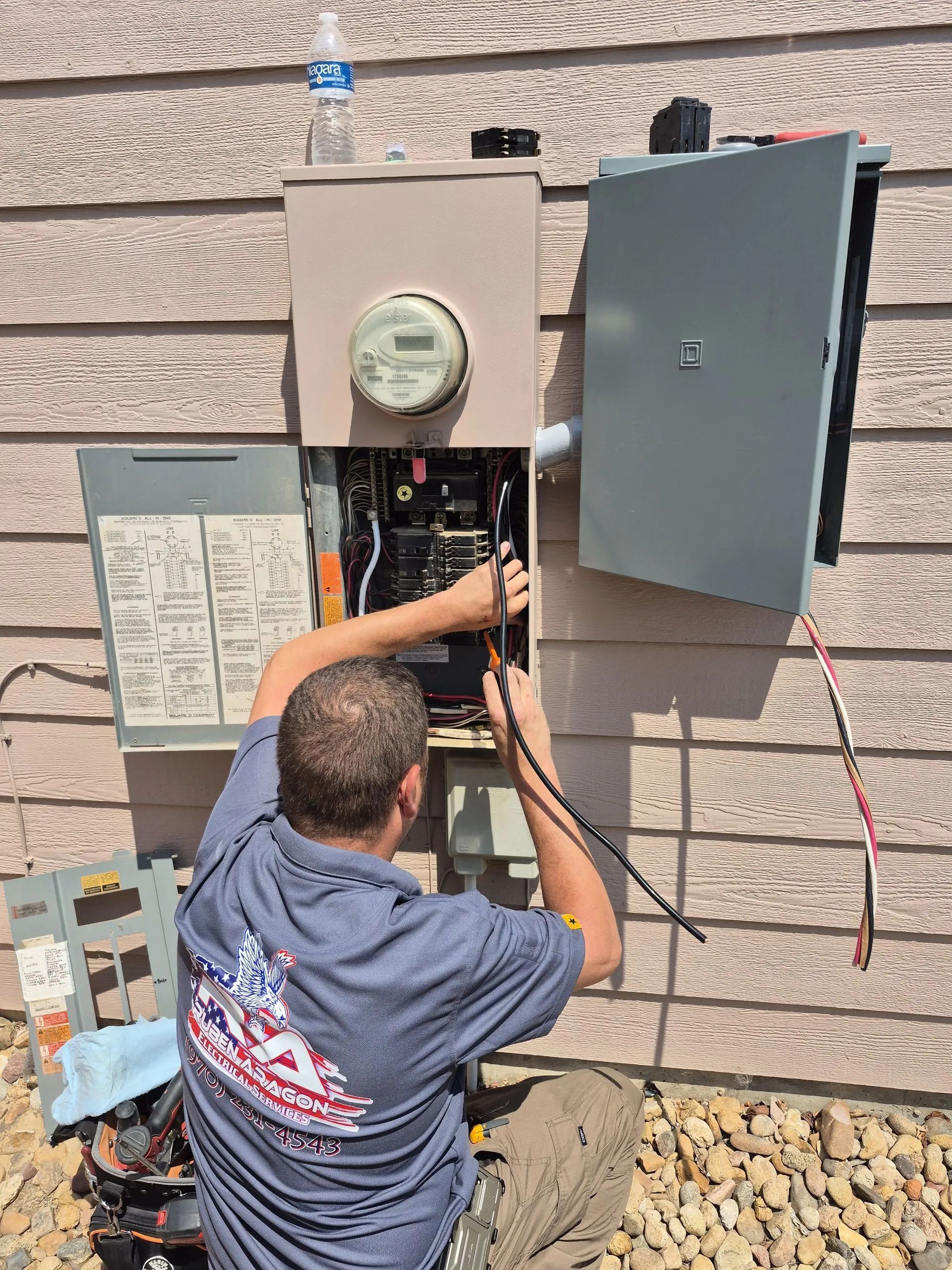 Electrician working on electrical panel mounted on a building's exterior.