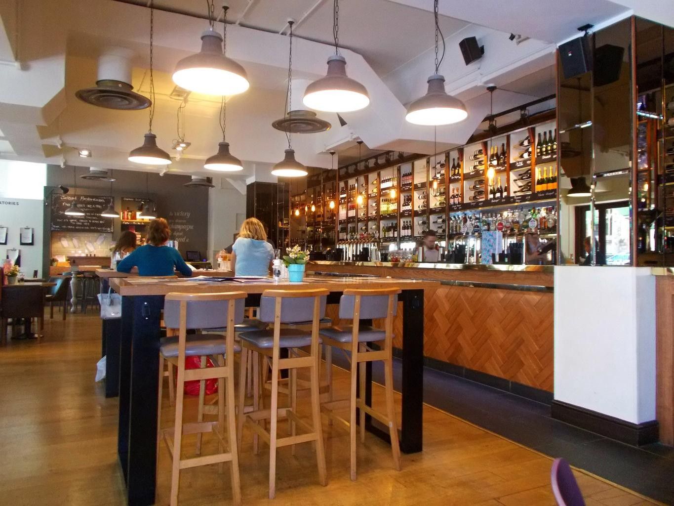 Interior of a bar with people seated at tables and bar. Overhead lights illuminate the space.