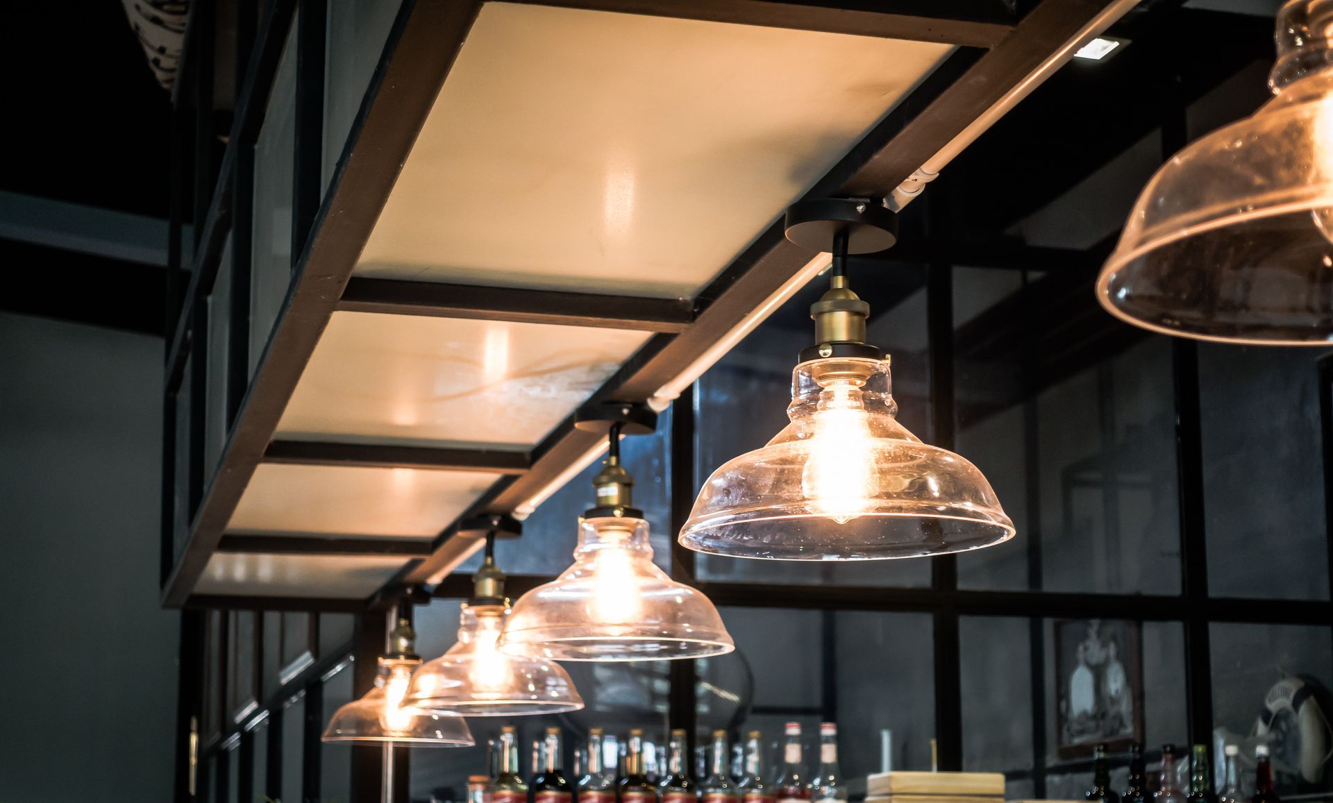 Row of illuminated glass pendant lights hanging from a dark beam, casting warm glow.