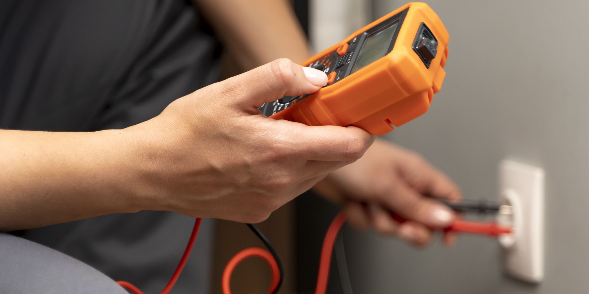 Person tests electrical outlet with orange multimeter.