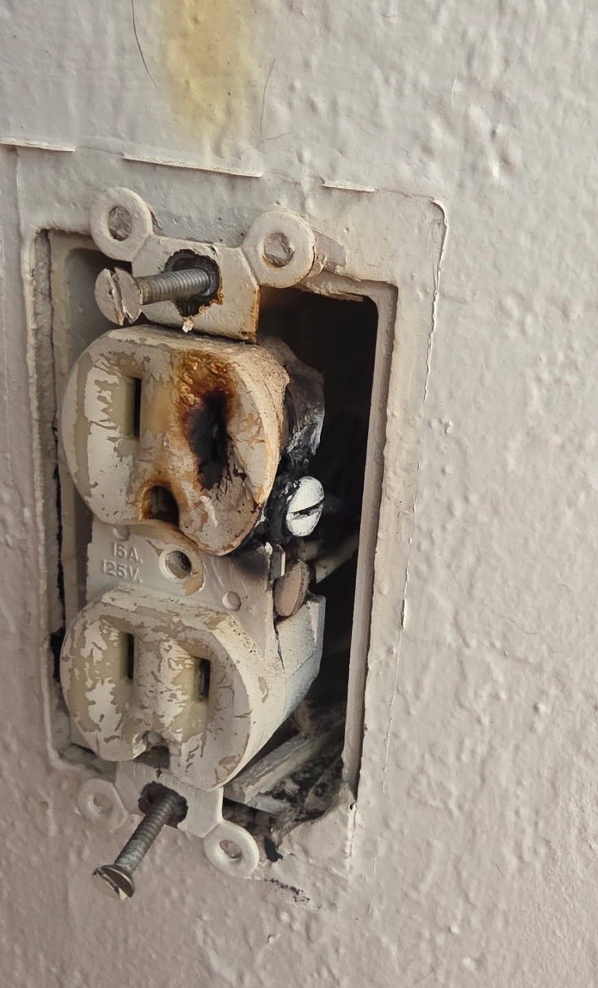 Burned electrical outlet in a white wall; black charring and damage are visible.