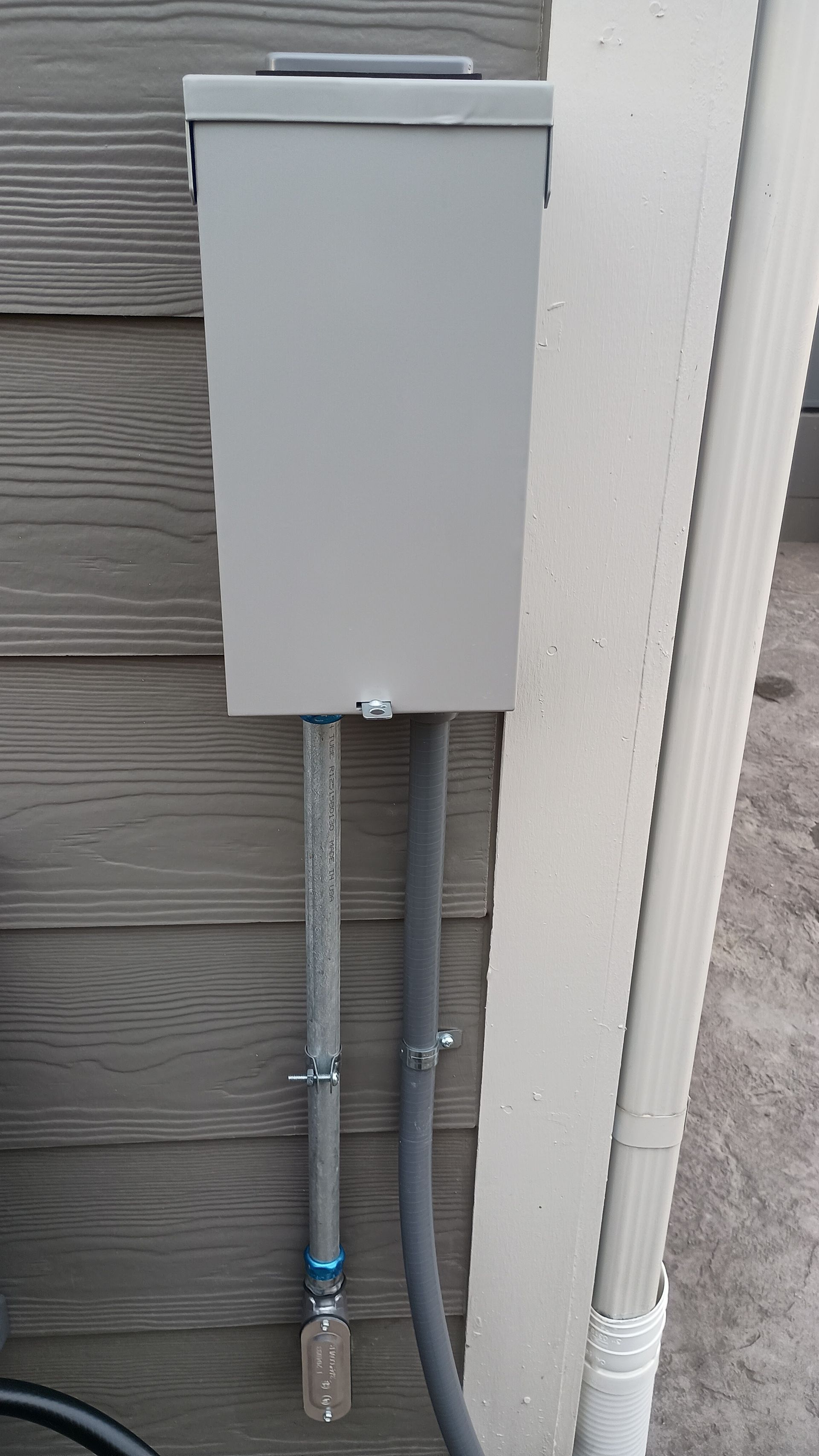 Gray electrical box mounted on a gray siding wall, with two conduits below.