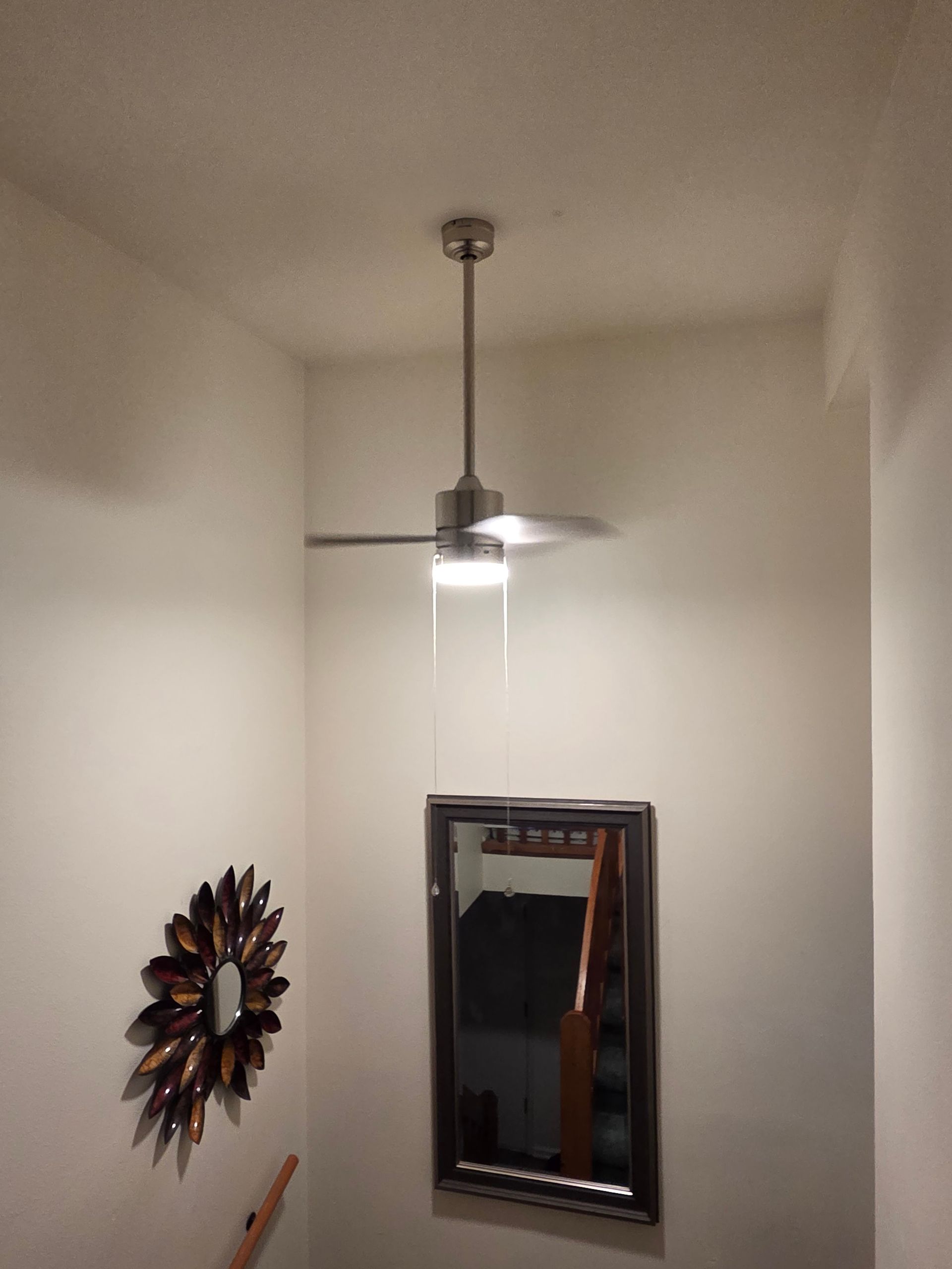 Ceiling fan above mirror and sunburst decor on a white wall in an entryway.
