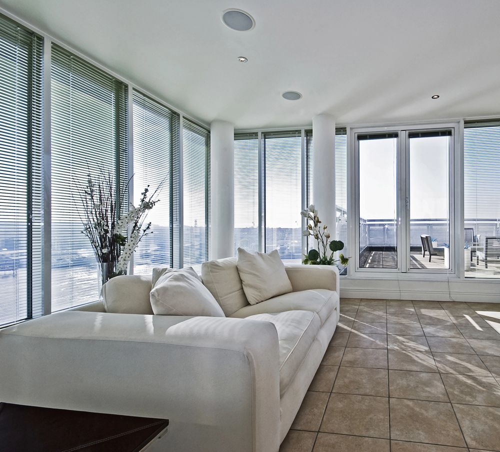 Soggiorno con divano bianco, ampie finestre con persiane e pavimento piastrellato.