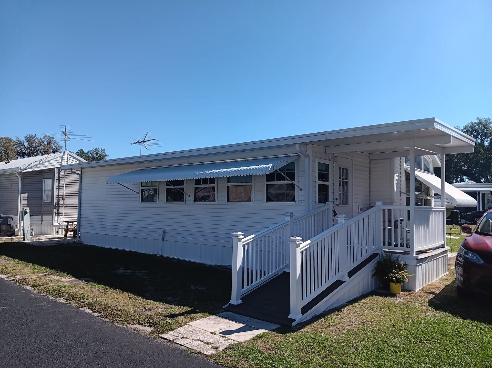 White mobile home with a ramp, awning, and blue sky.