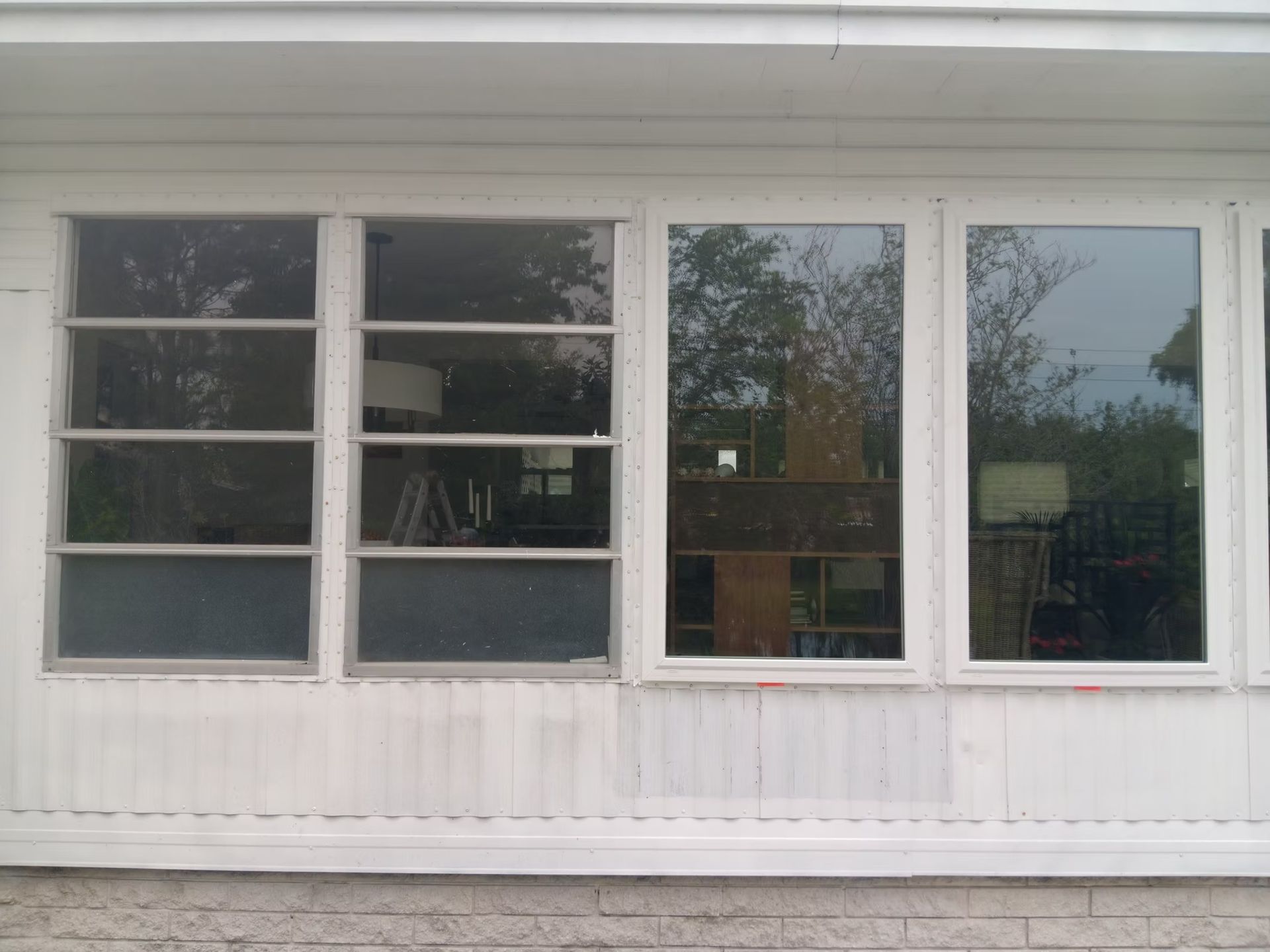 Four white-framed windows on a white house, reflecting the outdoors. Some grime visible on the siding.