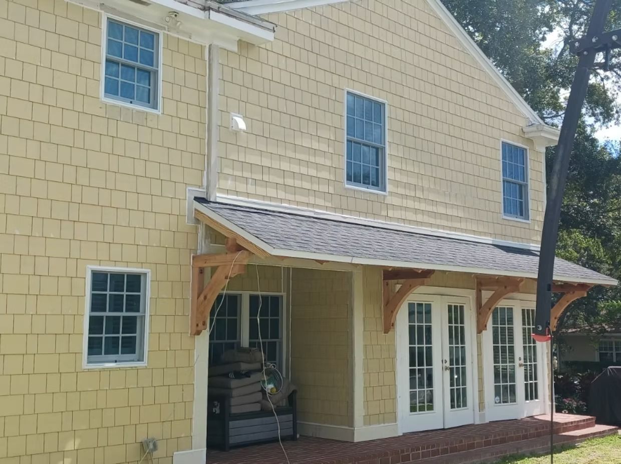 Yellow shingled house with a covered entryway and French doors. Wooden brackets support the roof.