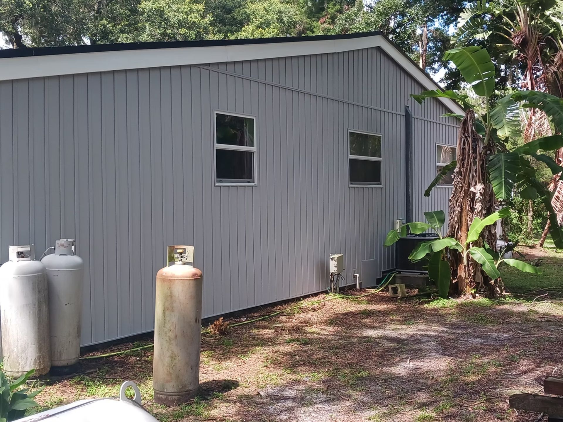 Gray building exterior with two windows, propane tanks, and foliage.