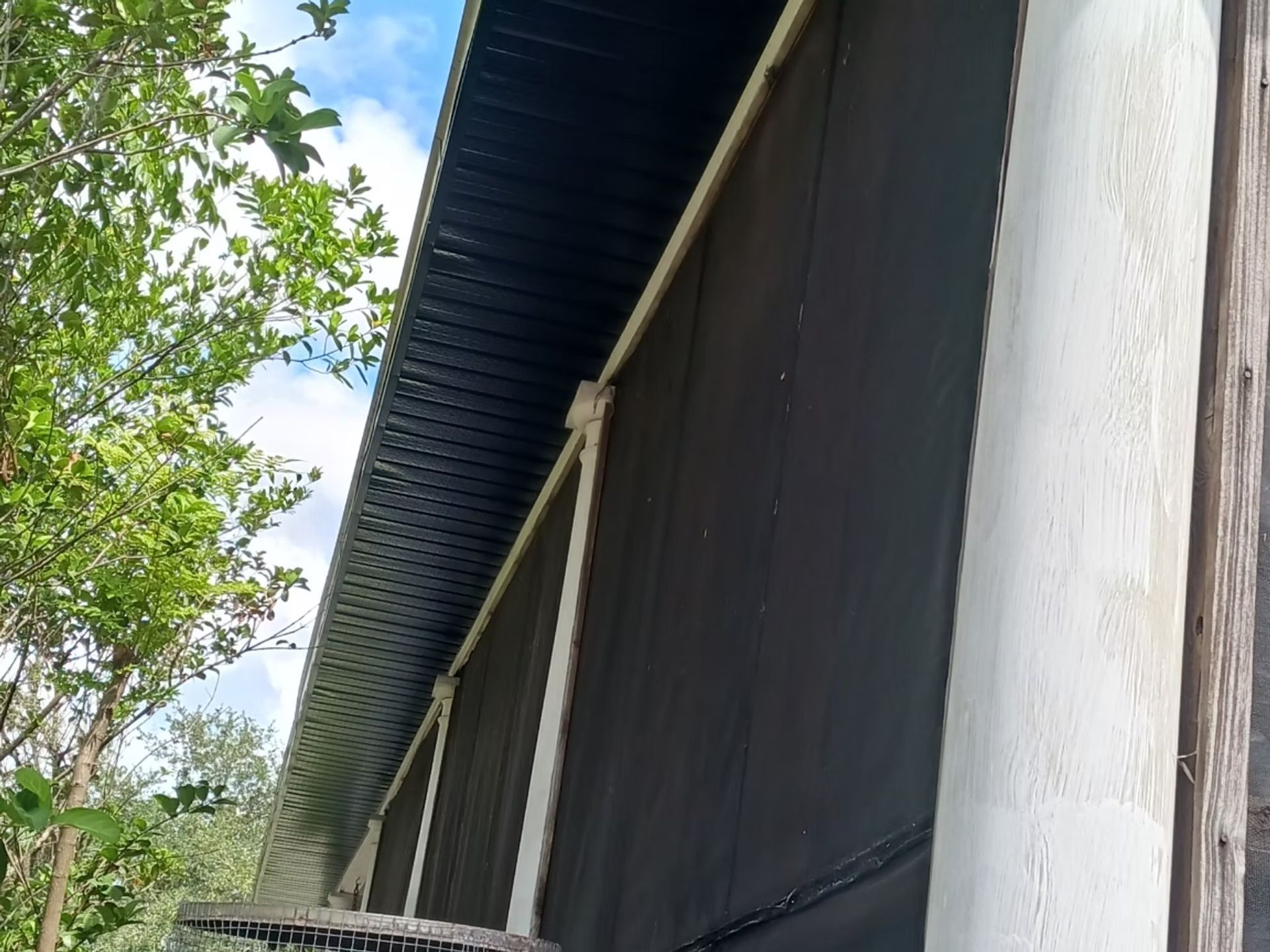 Side view of a building with a dark corrugated roof and dark siding; white support columns.