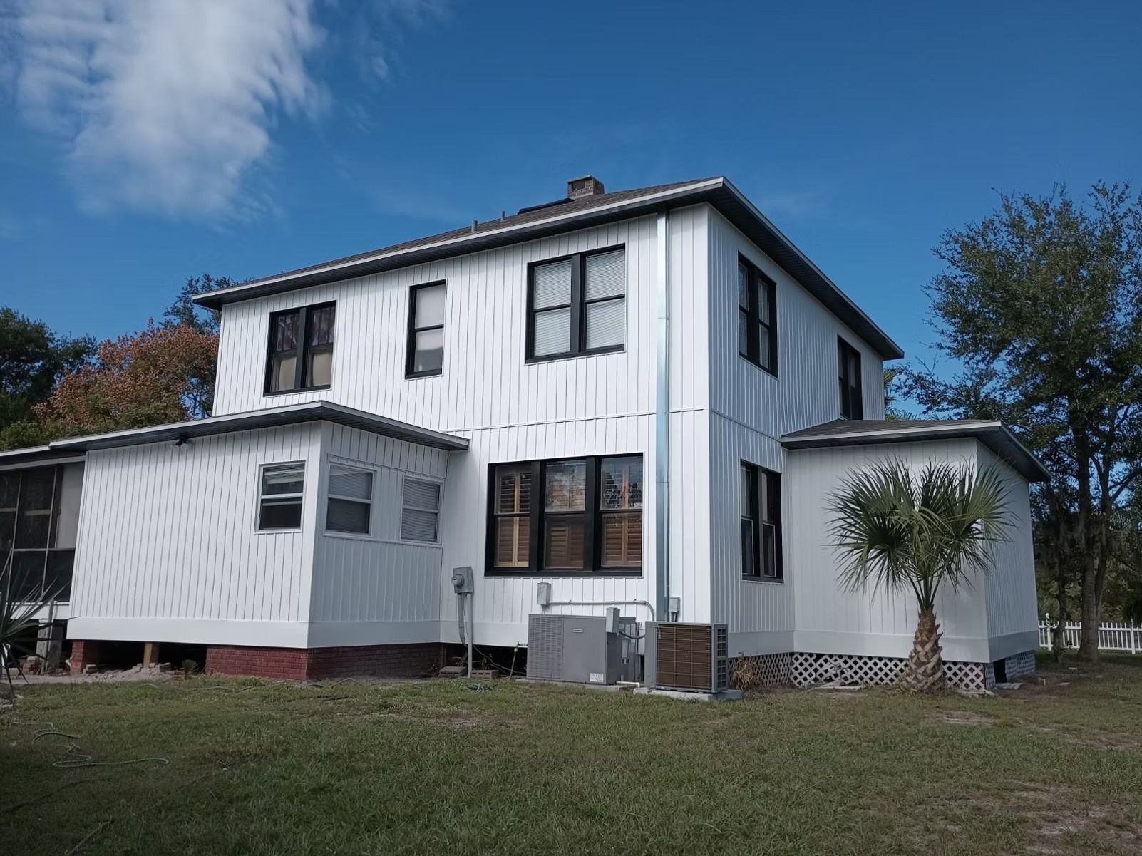 White two-story house with black-framed windows, surrounded by green grass and a blue sky with clouds.