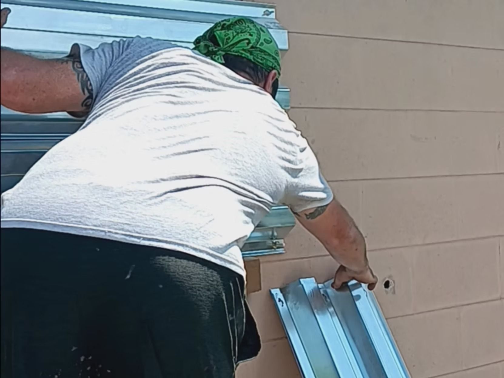 Person installing metal hurricane shutters on a light-colored building exterior.