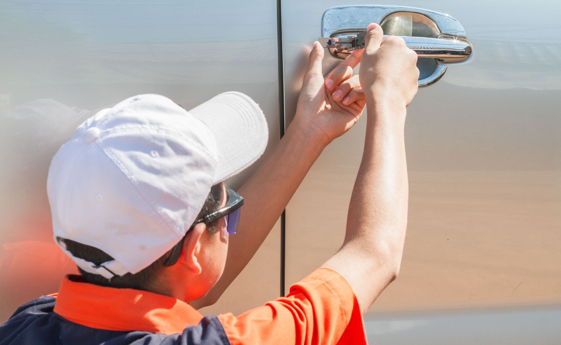 Person in white cap opening a car door handle, outdoors in sunlight.