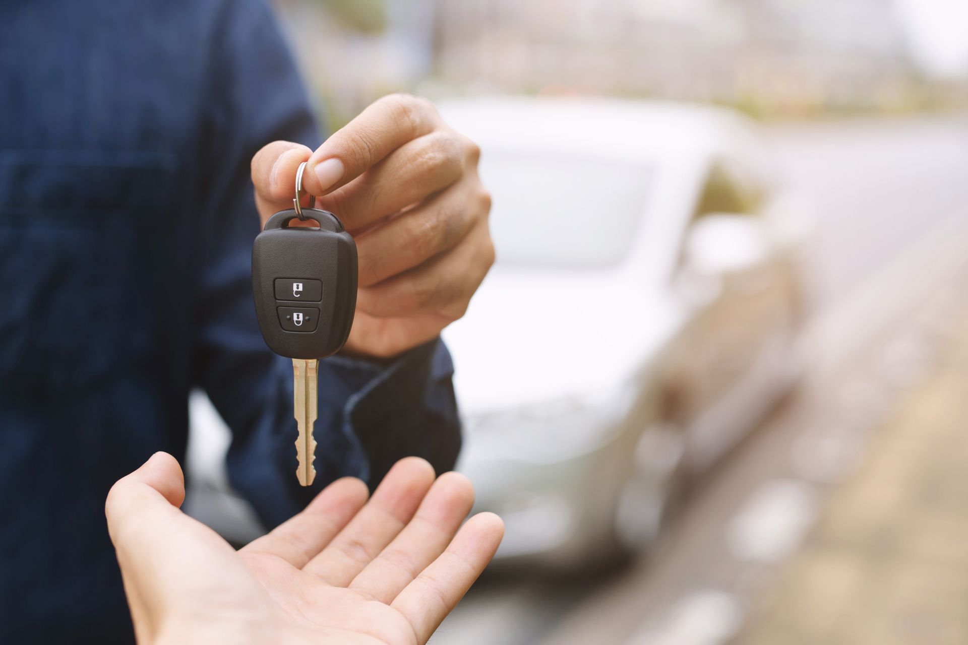 Hand holding car key, handing it to another open hand. 