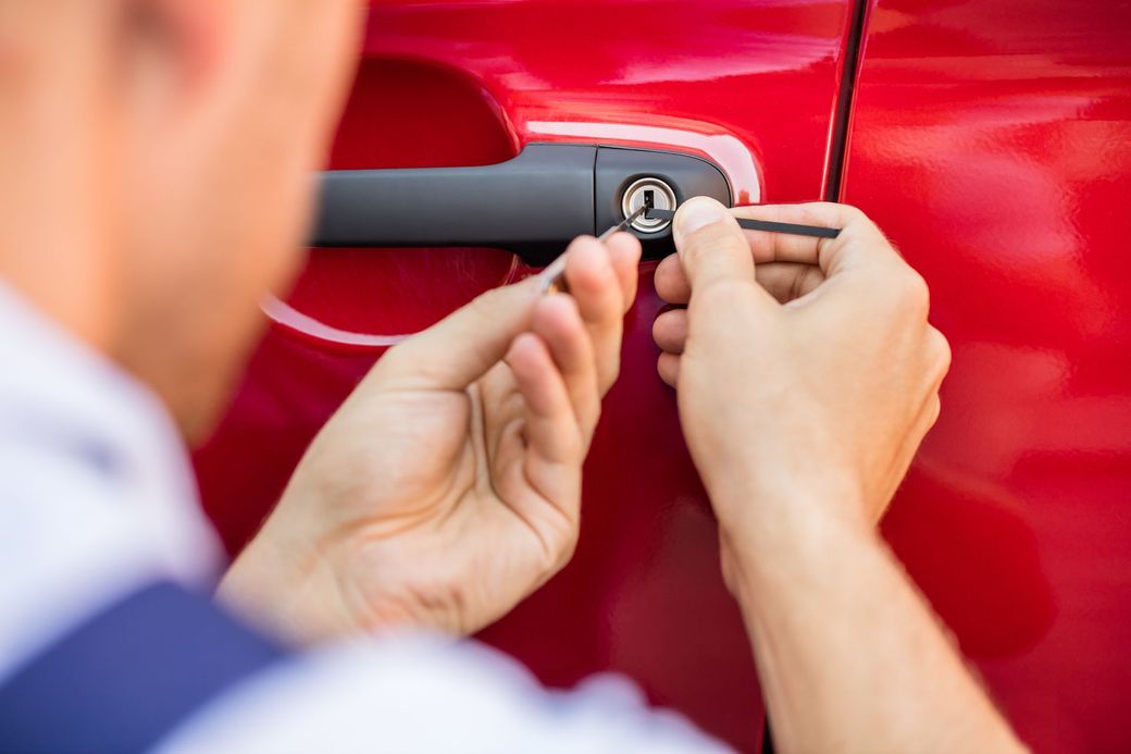 Person picking the lock of a red car door with small tools.