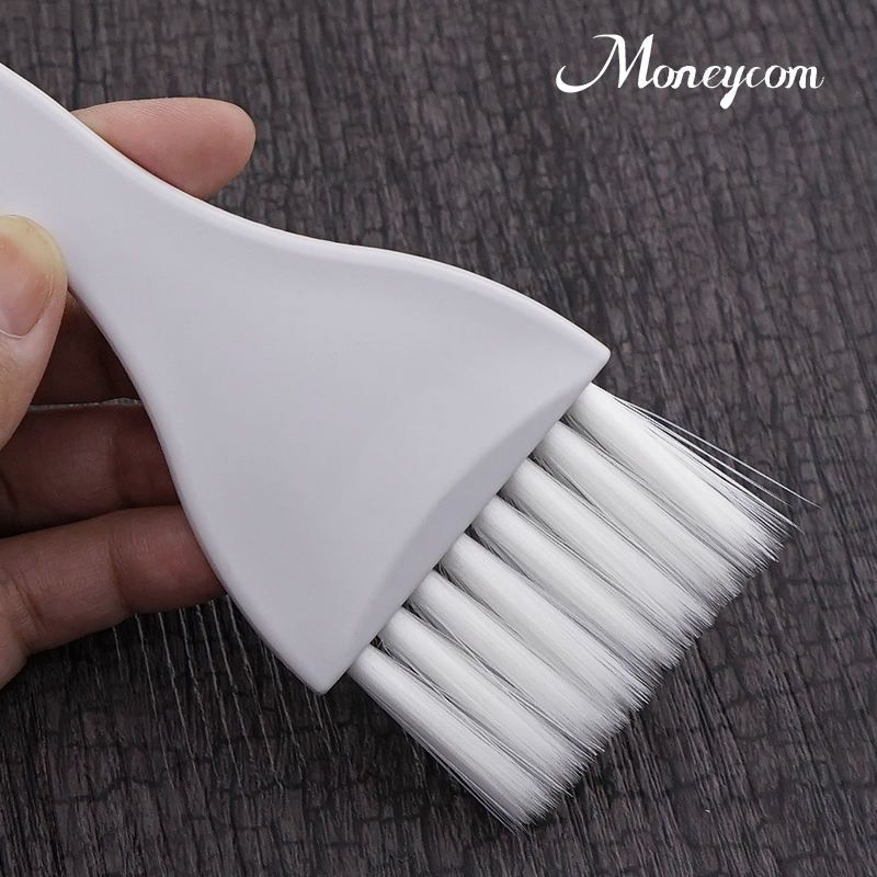 La mano de una persona sostiene un pincel aplicador de tinte para el cabello de plásticosobre un fondo oscuro texturizado.