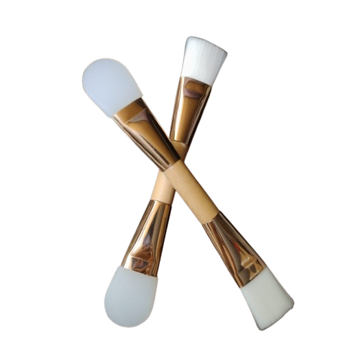 Dos brochas para mascarillas faciales de doble punta, dispuestas en forma de cruz sobre una superficie blanca.