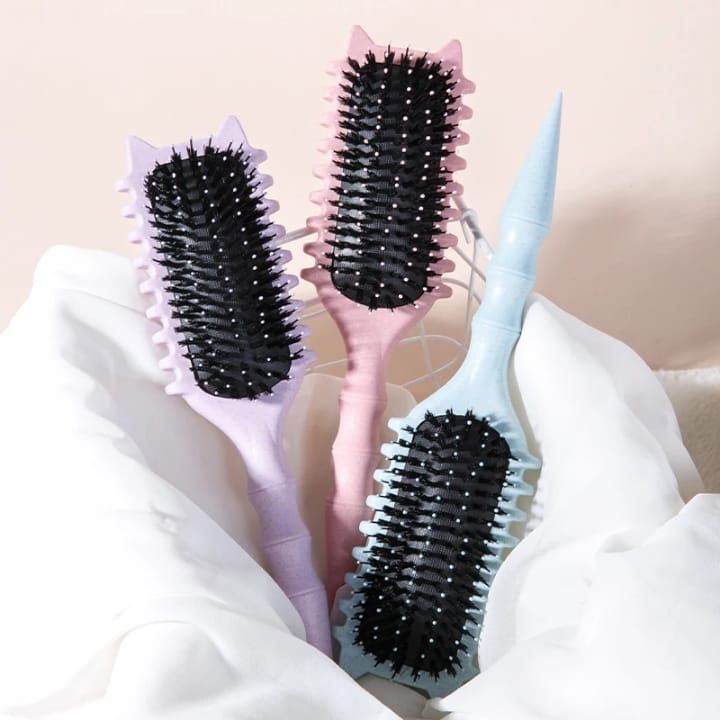 Tres cepillos rectangulares para el cabello con puntas en forma de orejas de gato, colocados sobre una suave tela blanca.