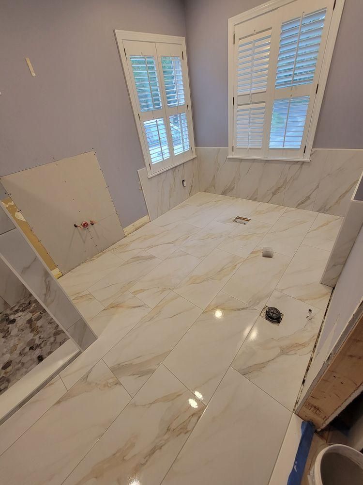Partially tiled bathroom floor with large white marble-look tiles and windows with shutters.