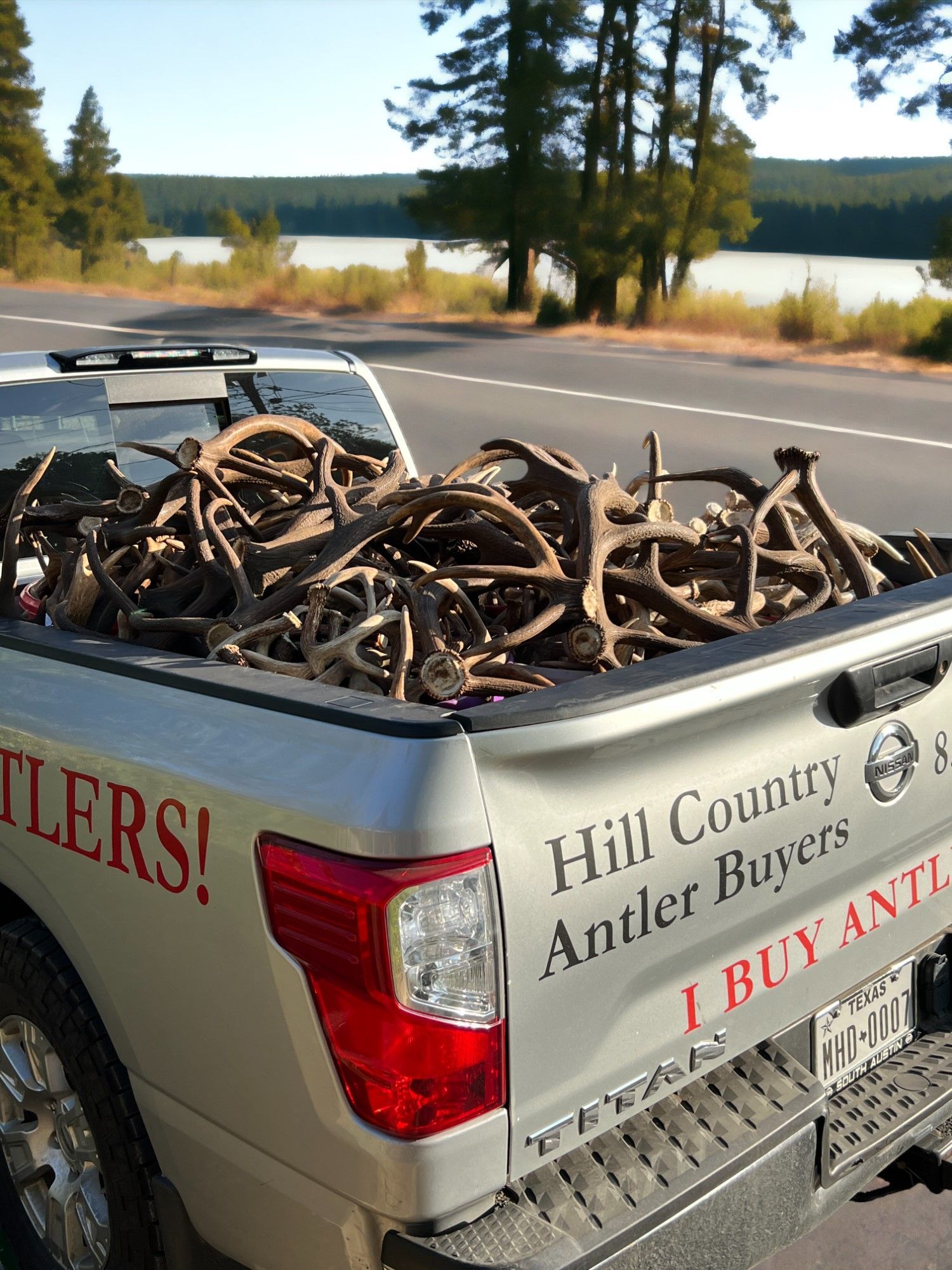 Truck bed filled with antlers, parked on a road beside a lake;