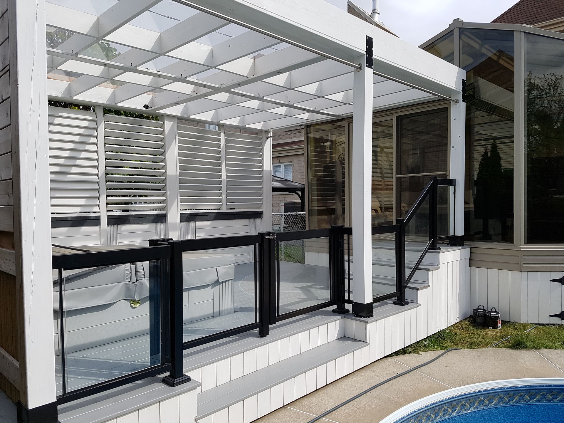 Une terrasse avec une pergola et une balustrade en verre à côté d'une piscine.