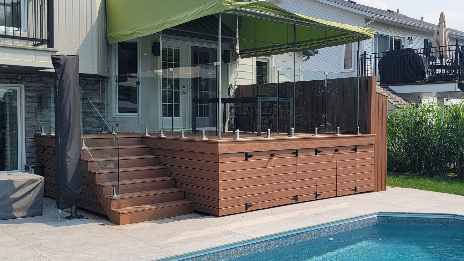 Une terrasse avec un auvent vert au-dessus à côté d'une piscine.