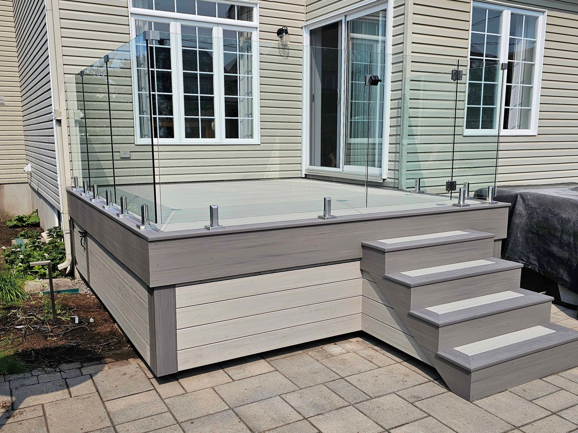 Une terrasse avec des escaliers et une balustrade en verre devant une maison.