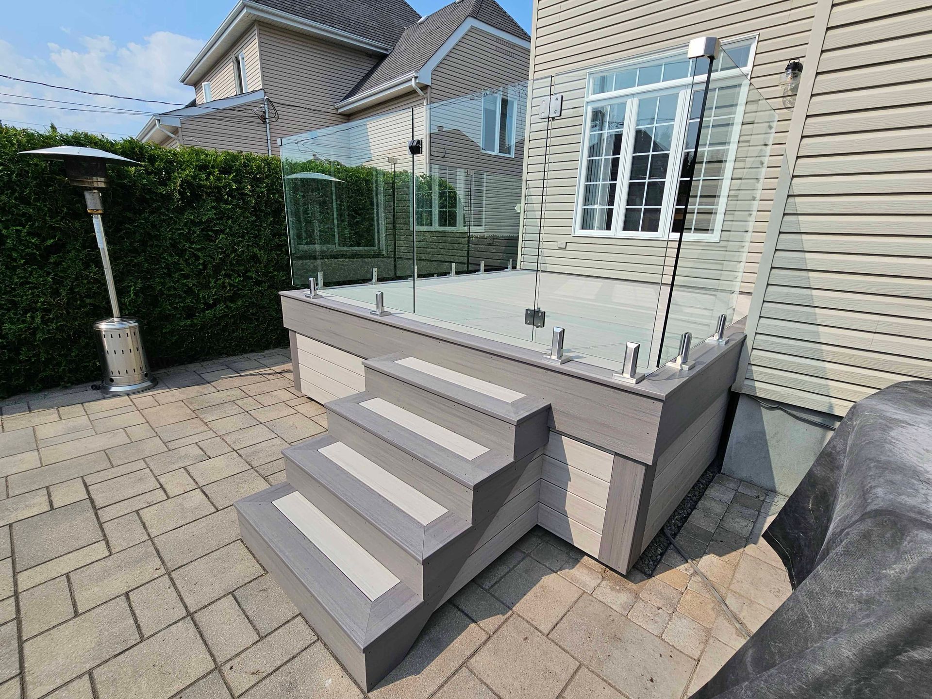 Un patio avec escalier et garde-corps en verre devant une maison.