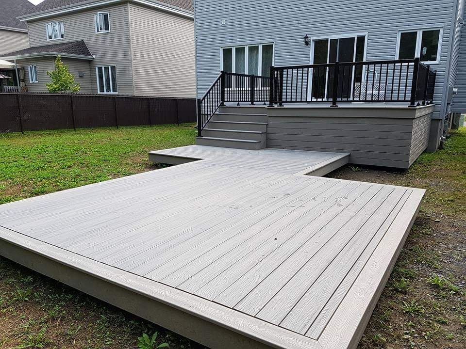 Une grande terrasse grise avec des escaliers se trouve dans l'arrière-cour d'une maison.