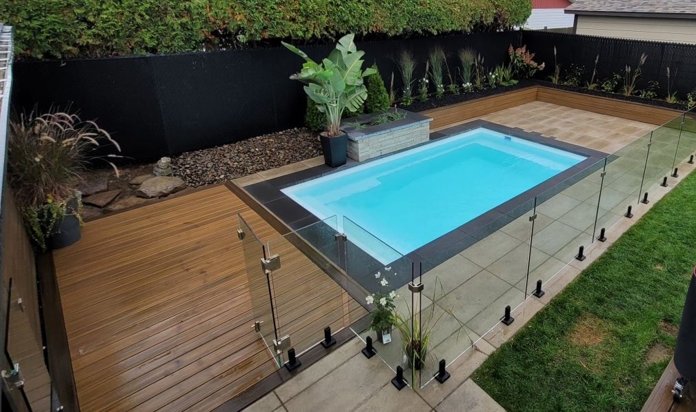 Une petite piscine est entourée d'une clôture en verre dans une arrière-cour.