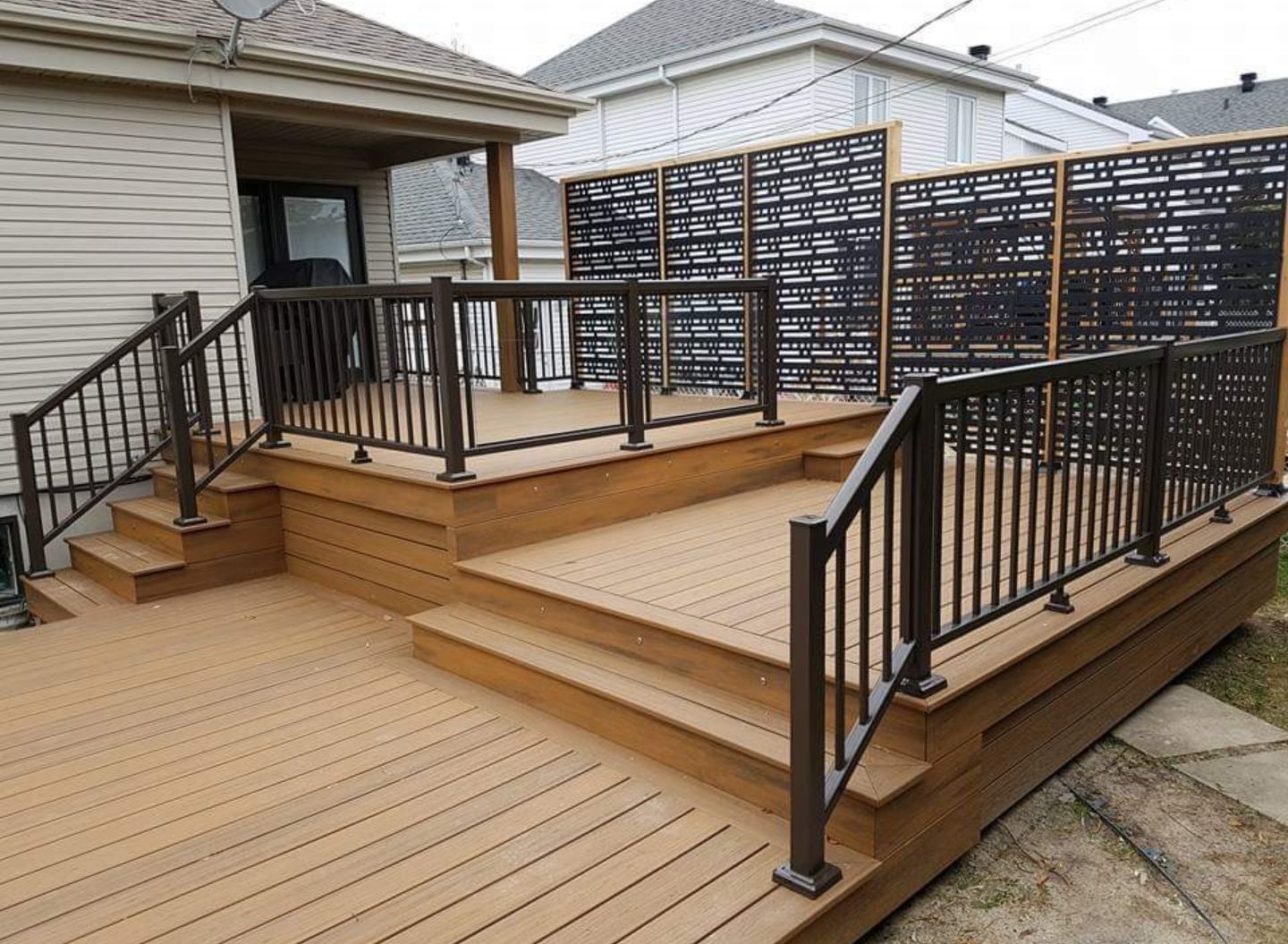 Une terrasse avec des escaliers et une balustrade en métal devant une maison.