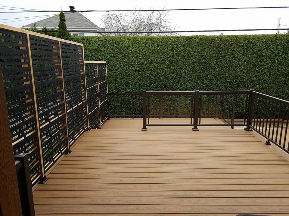 Une terrasse avec une balustrade en métal et une haie en arrière-plan.