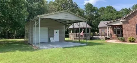 A carport is sitting in the middle of a lush green field next to a house.