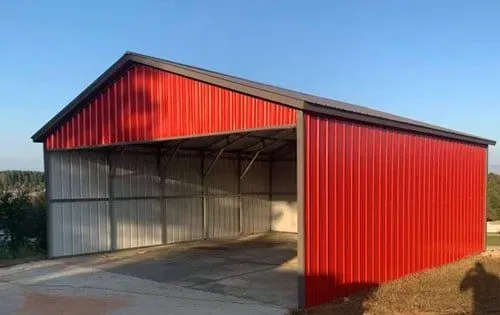 A red metal building with a brown roof is sitting on top of a dirt field.
