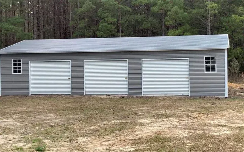 A large metal garage with three garage doors is sitting in the middle of a field.
