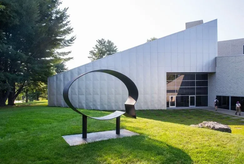 Sculpture in front of a modern art museum. Black metal loop on green grass. Light-colored building.