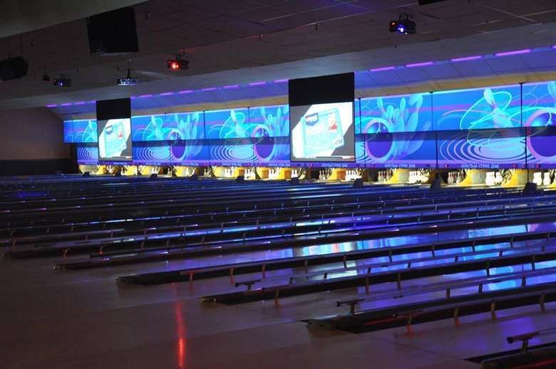 Bowling alley with rows of lanes, screens displaying graphics, and purple lighting.