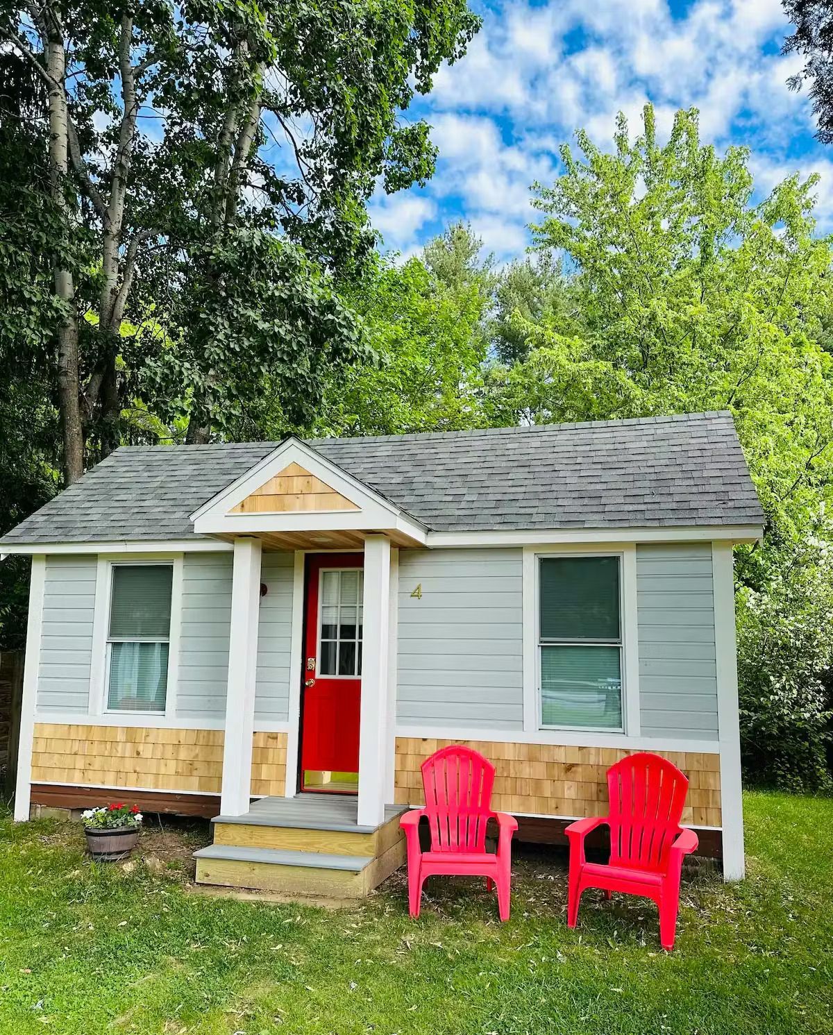 Small gray cottage with red door, cedar shingling, two red chairs on the lawn.