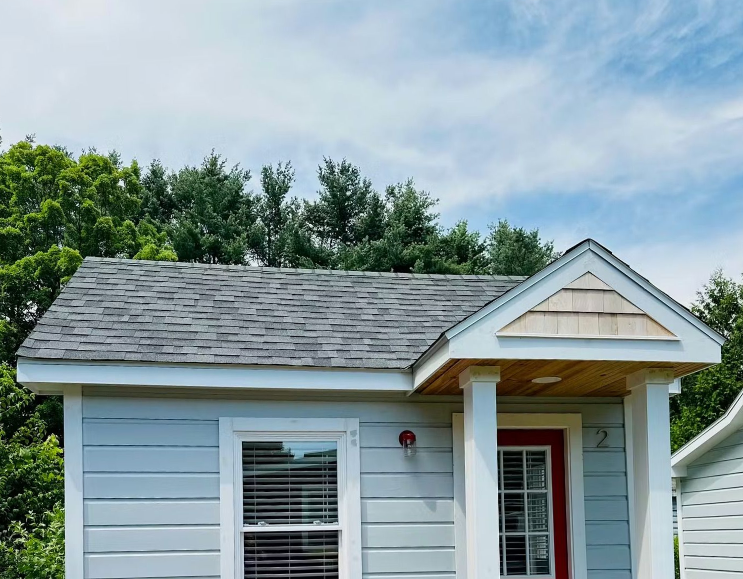 Small blue house with gray roof, white columns, red door, and window under a blue sky.